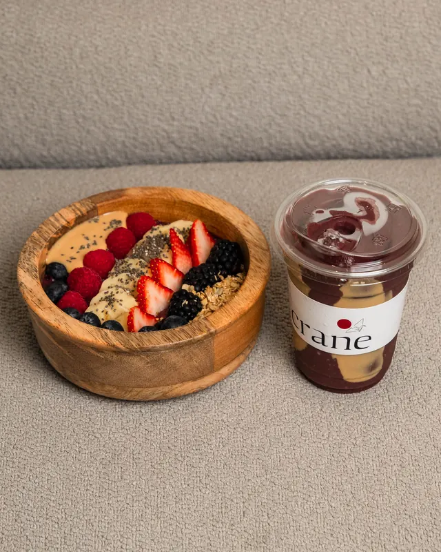 An açaí bowl topped with berries next to a Crane iced drink