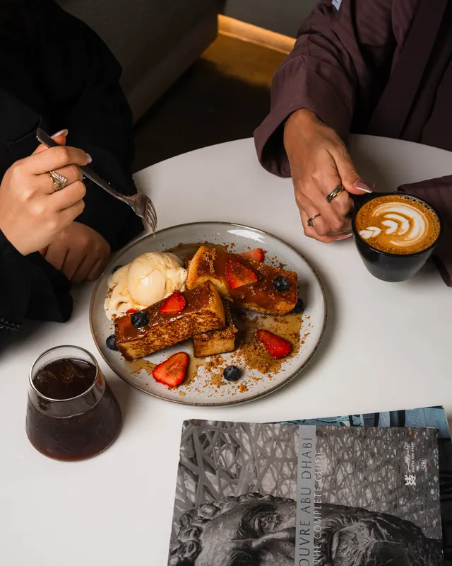 Two friends sharing French toast and lattes at a round table