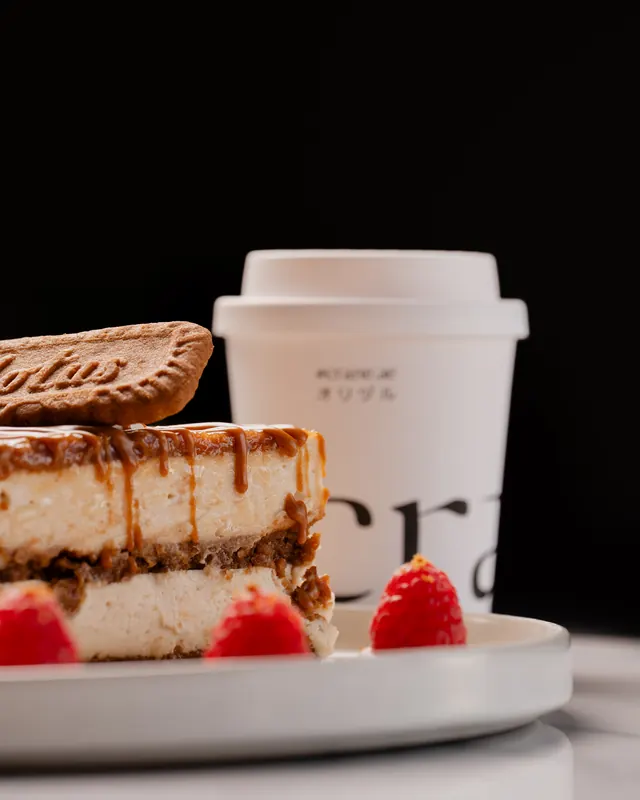 A layered caramel biscuit cake with strawberries beside a Crane cup
